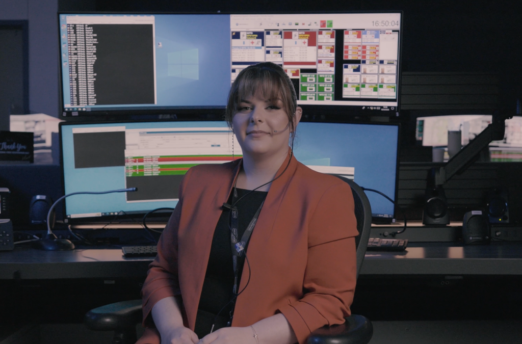 female 9-1-1 telecommunicator with a headset on sitting in front of her workspace at a call center